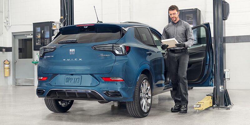Man with Safety Glasses and White Papers Walking Next to Blue Buick SUV