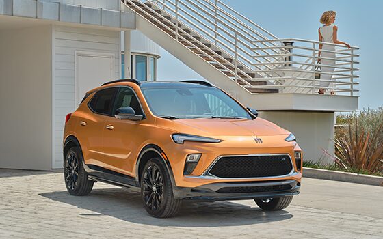 Orange Buick Parked in Sand Next to a Building with a Woman Standing on the Exterior Staircase