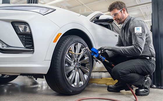 Male Technician Bending Down Working on the Tire of White Vehicle