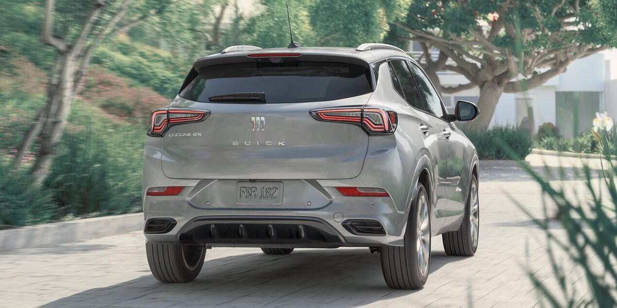 Back view of the 2025 Buick Encore GX Avenir driving on a tree-lined road.