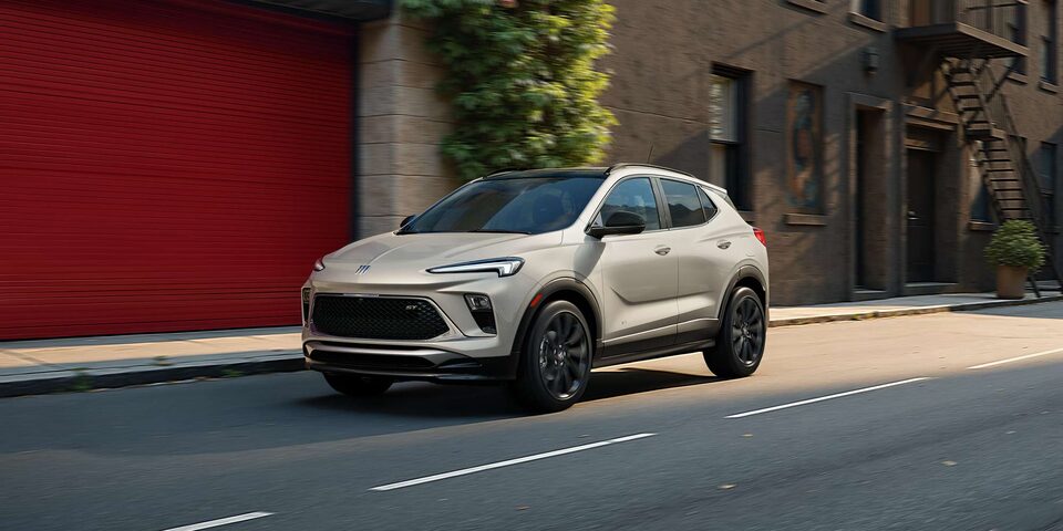 The 2026 Buick Encore GX Sports Touring SUV in the Color Ceramic Driving Down a City Street