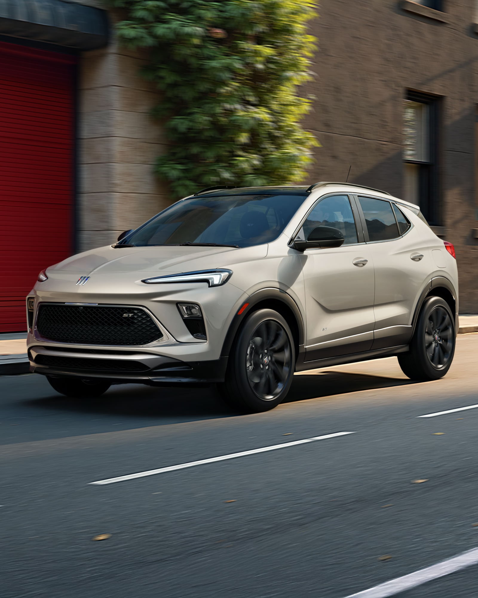 The 2026 Buick Encore GX Sports Touring SUV in the Color Ceramic Driving Down a City Street