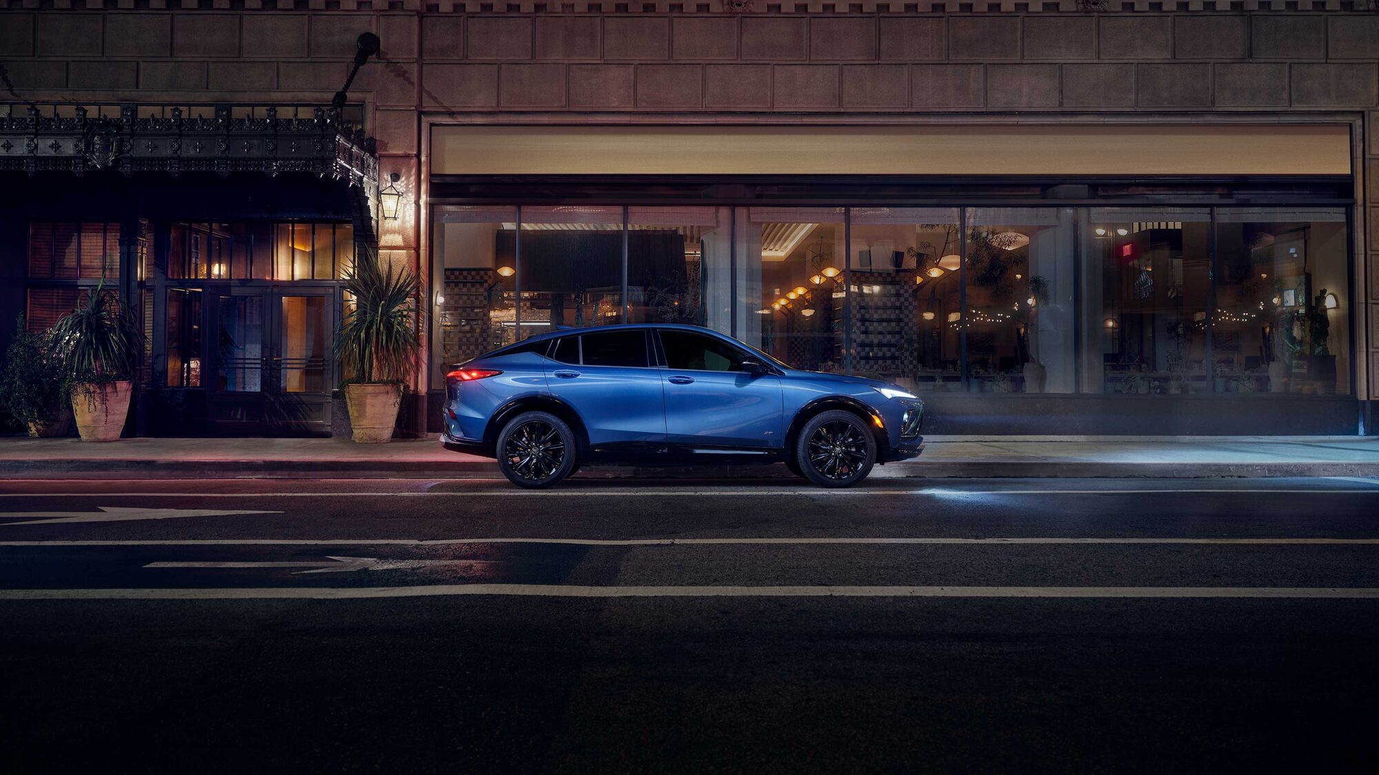 Side View of a Blue 2026 Buick Envista Sport Touring Sport SUV Driving Through Downtown at Night