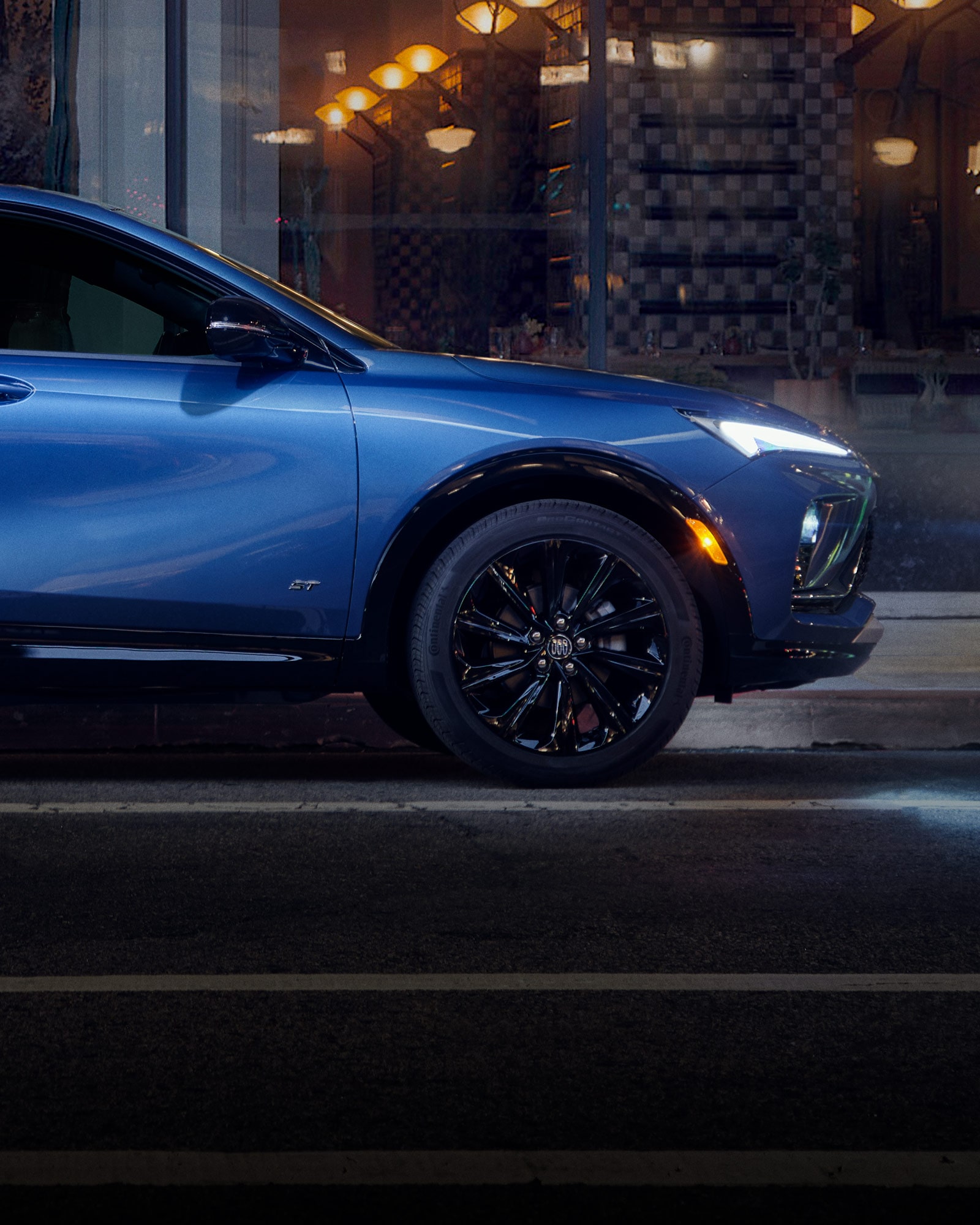 Side View of a Blue 2026 Buick Envista Sport Touring Sport SUV Driving Through Downtown at Night