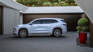 Un VUS Buick Enclave blanc 2027 stationné à côté d’un bâtiment moderne avec des portes de garage sombres