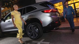 Un homme et une femme passant devant un VUS Buick Enclave gris 2027 dans une rue de la ville la nuit