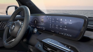 Vue rapprochée du tableau de bord de la Buick Enclave 2027 avec un grand écran numérique courbé et un horizon océanique en arrière-plan.